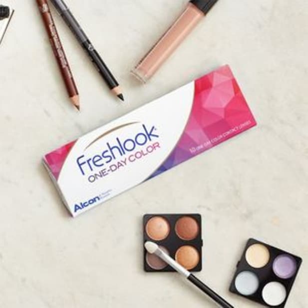 Eine Packung Freshlook One-Day Color Farblinsen neben Lidschattenpaletten, Kajalstiften und Concealer
